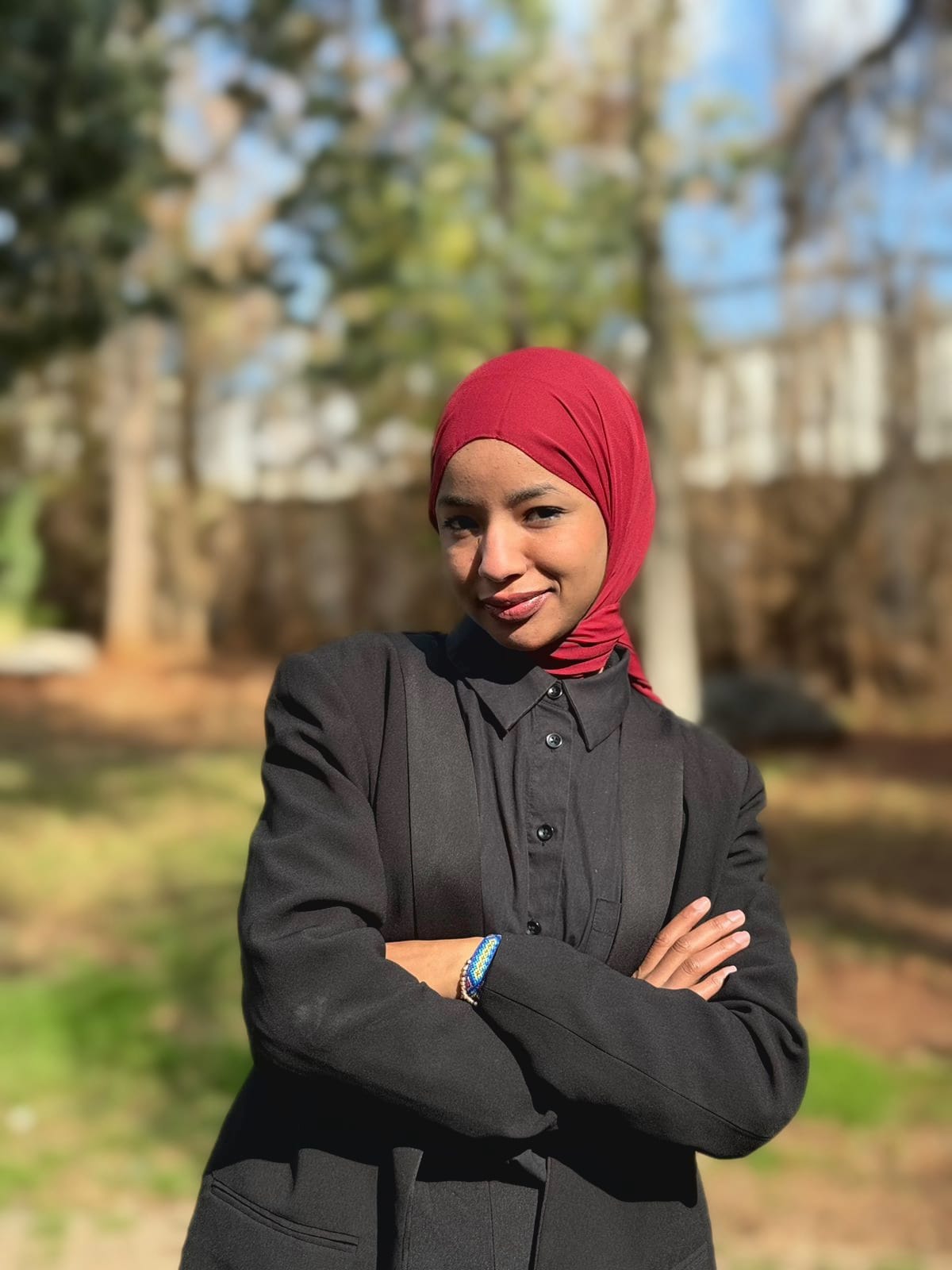 Imane outdoors, wearing a red scarf and black blazer